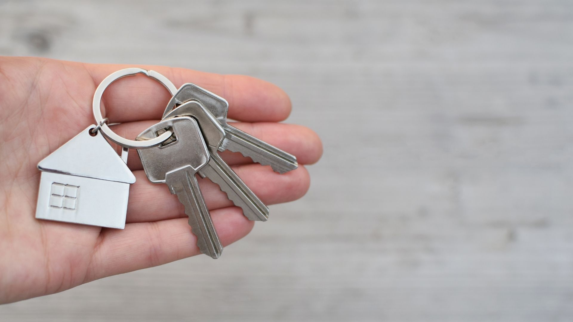 Plan sur une main qui porte un trousseau de clé avec un porte-clé en forme de maison